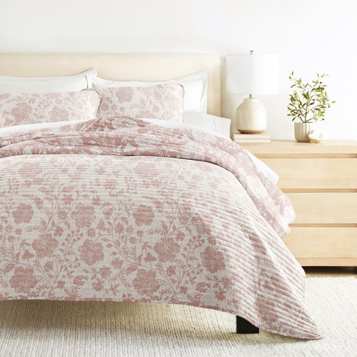 Floral-patterned bedding with lamp on wooden nightstand.