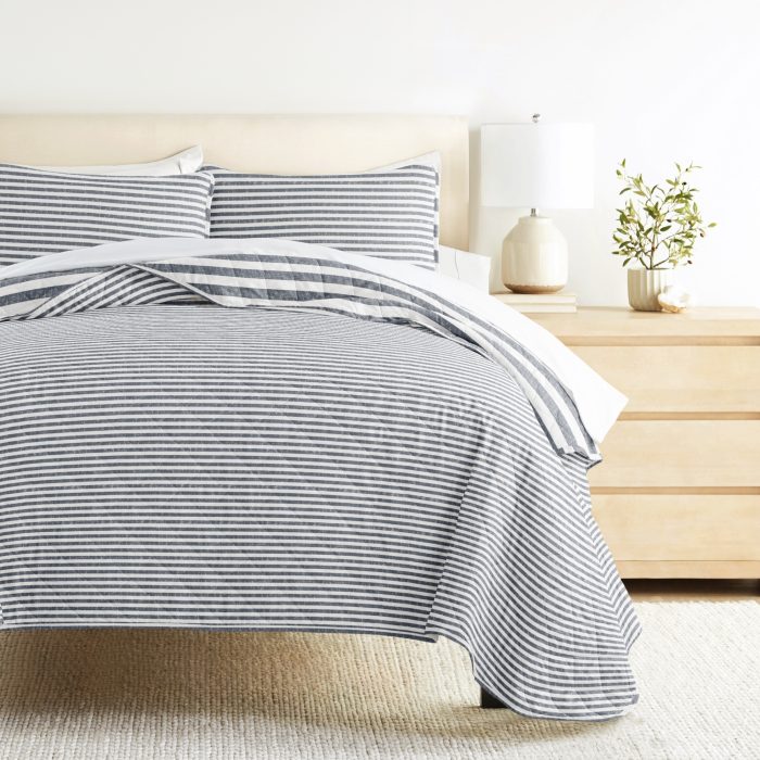 Striped bedding with lamp and plant on nightstand.